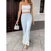 Woman wearing a white top and light blue pants with lace details, standing on a tiled floor.